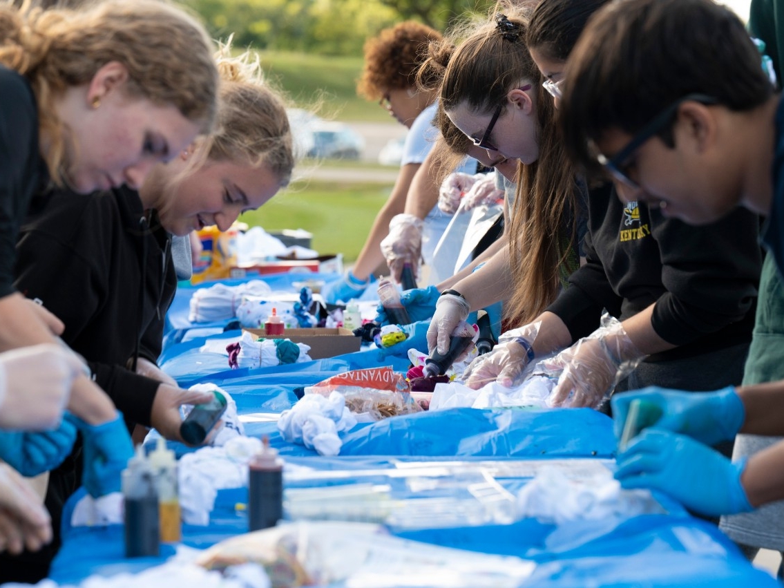 A large group of NKU STEM students intently dying their t-shirts outside on a beautiful, sunny day.