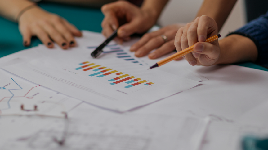 Two people holding pens point at a set of graphs