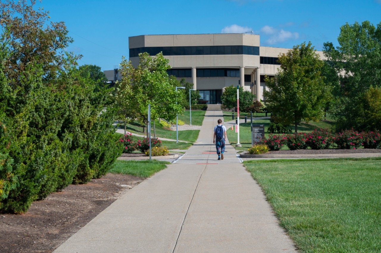 A student walks on the side walk toward the Haile College of Business building.